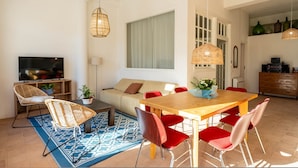 A modern living room with a sofa, a wooden dining table, red chairs, wicker chairs, a TV, and a large window with curtains. - Casa Tharros in Nurachi (Nurachi)