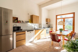 Une cuisine moderne dotée d’un réfrigérateur en acier inoxydable, de meubles en bois, d’un four à micro-ondes encastré et d’un coin repas avec des chaises rouges.