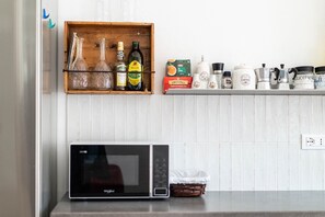 Una encimera de cocina con un microondas, una repisa de madera con botellas y una caja de té Twinings English Breakfast.