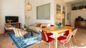 A modern living room with a sofa, dining table, chairs, a TV, and decorative items. - Casa Tharros Apartment Garden (Nurachi)