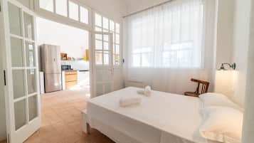Un dormitorio con una cama, una silla de madera, una mesita de noche y una ventana con cortinas.