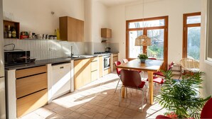 A modern kitchen with wooden cabinets, a built-in dishwasher, and a dining area with a table and chairs. - Casa Tharros Apartment Garden (Nurachi)