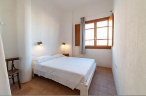 Una habitación pequeña y limpia con una cama individual, una silla de madera, una mesita de noche y una ventana con cortinas.