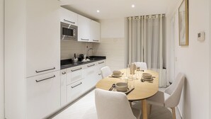 A modern kitchen with white cabinetry, a microwave, and a dining area with a wooden table and chairs. - Galea Studio by Wonderful Italy (Genoa)