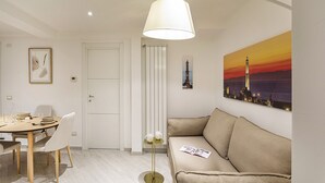 A modern living room with a beige sofa, a dining table with chairs, a floor lamp, and a painting of a cityscape. - Galea Studio by Wonderful Italy (Genoa)