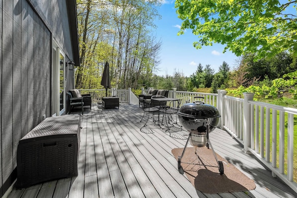 Une terrasse en bois avec des meubles dâextĂ©rieur, un barbecue et une rambarde blanche.
