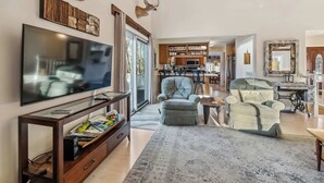 Ein geräumiges Wohnzimmer mit einem großen Flachbildfernseher, einer Holzunterhaltungsecke und zwei gepolsterten Sesseln.