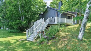 Ein zweistöckiges Haus mit einer Holztreppe, die zu einer Terrasse führt, umgeben von üppigem Grün.