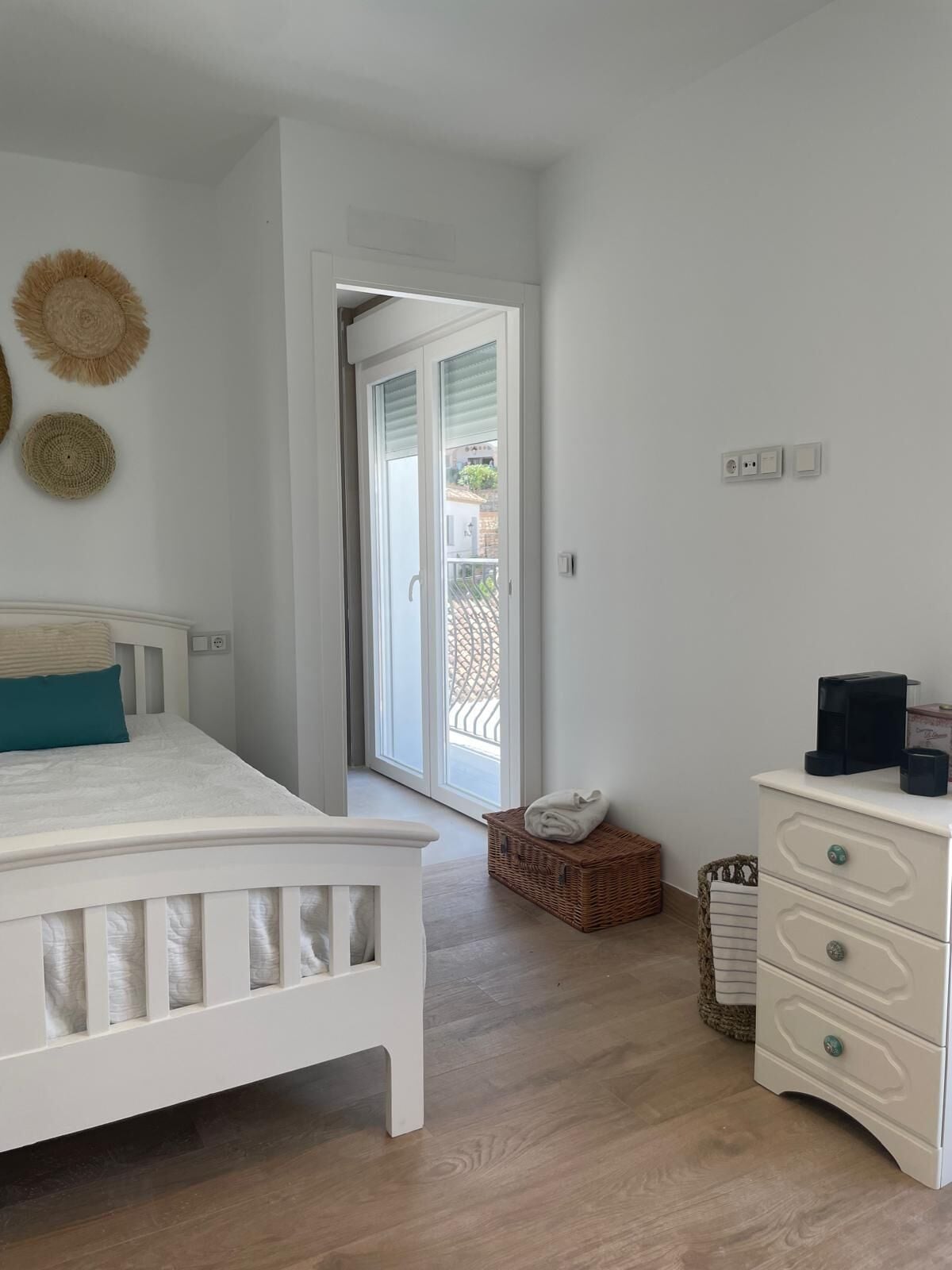 Un dormitorio con cama, cómoda, cesta y puerta que da a un balcón.