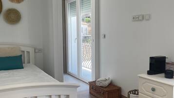 Un dormitorio con cama, cómoda, cesta y puerta que da a un balcón.