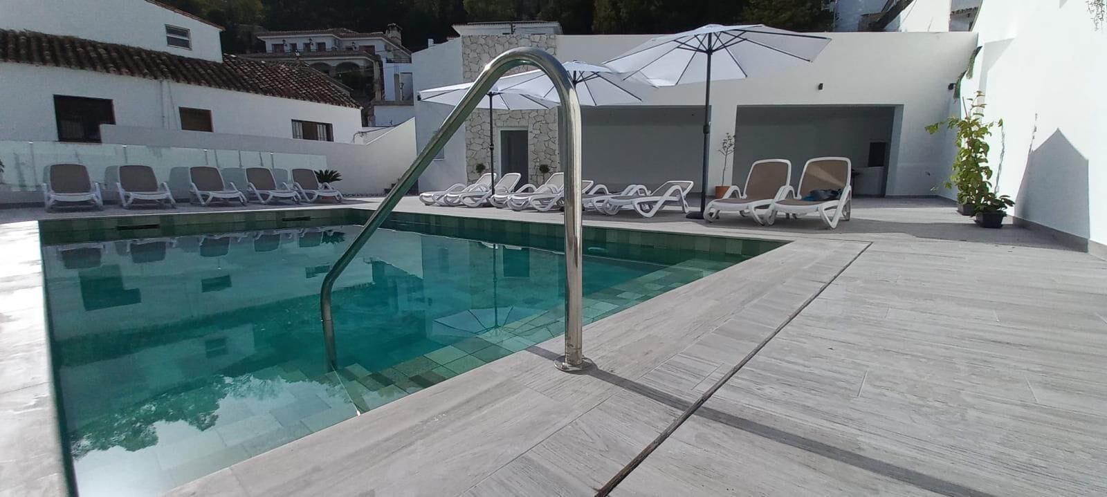 Una piscina con una escalera de metal, rodeada de sillas de descanso y sombrillas.