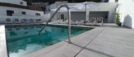 A swimming pool with a metal ladder, surrounded by lounge chairs and umbrellas.