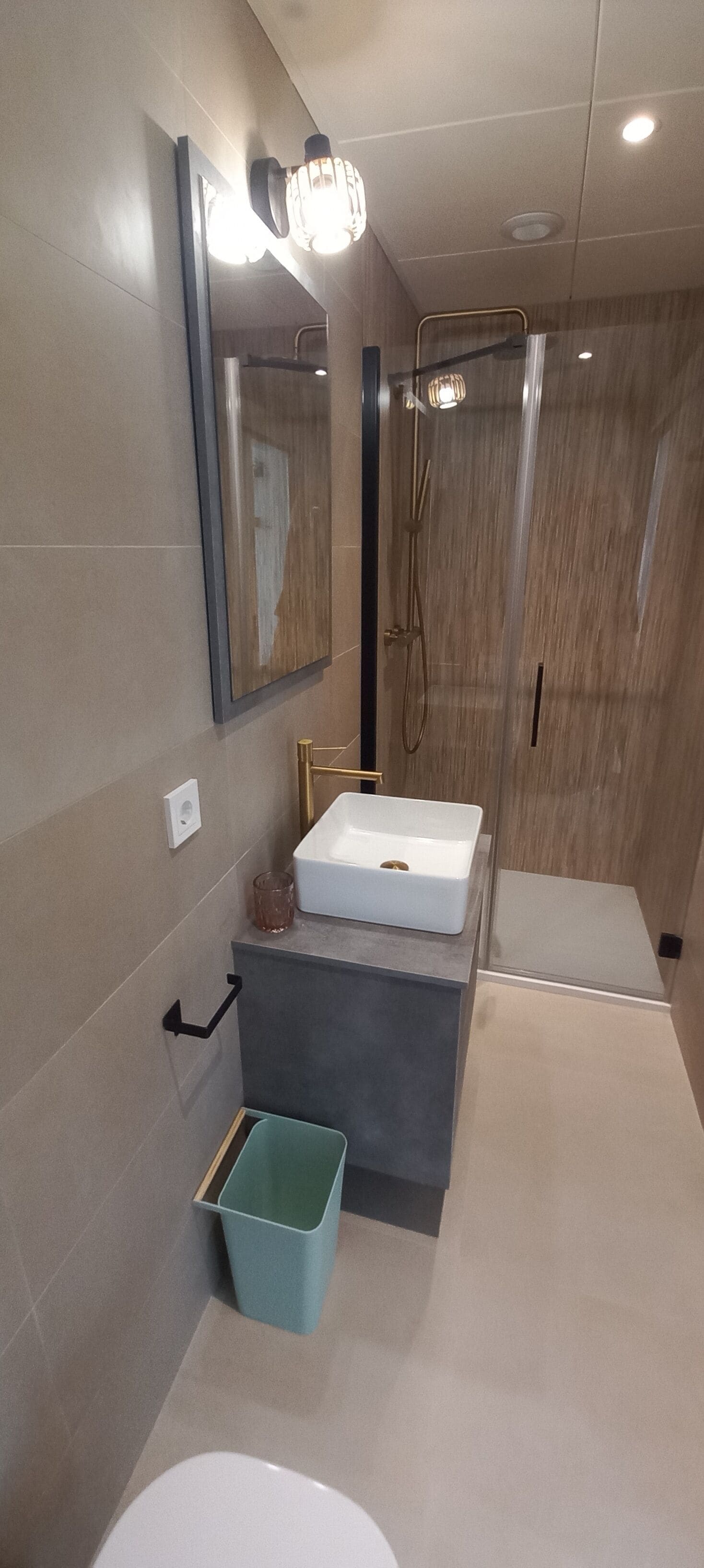 Een moderne badkamer met een grote spiegel, een witte wastafel, een douchegedeelte en een prullenbak.
