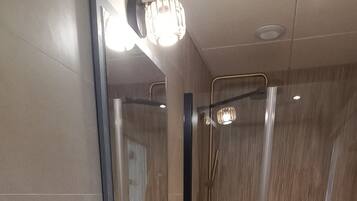 Een moderne badkamer met een grote spiegel, een witte wastafel, een douchegedeelte en een prullenbak.