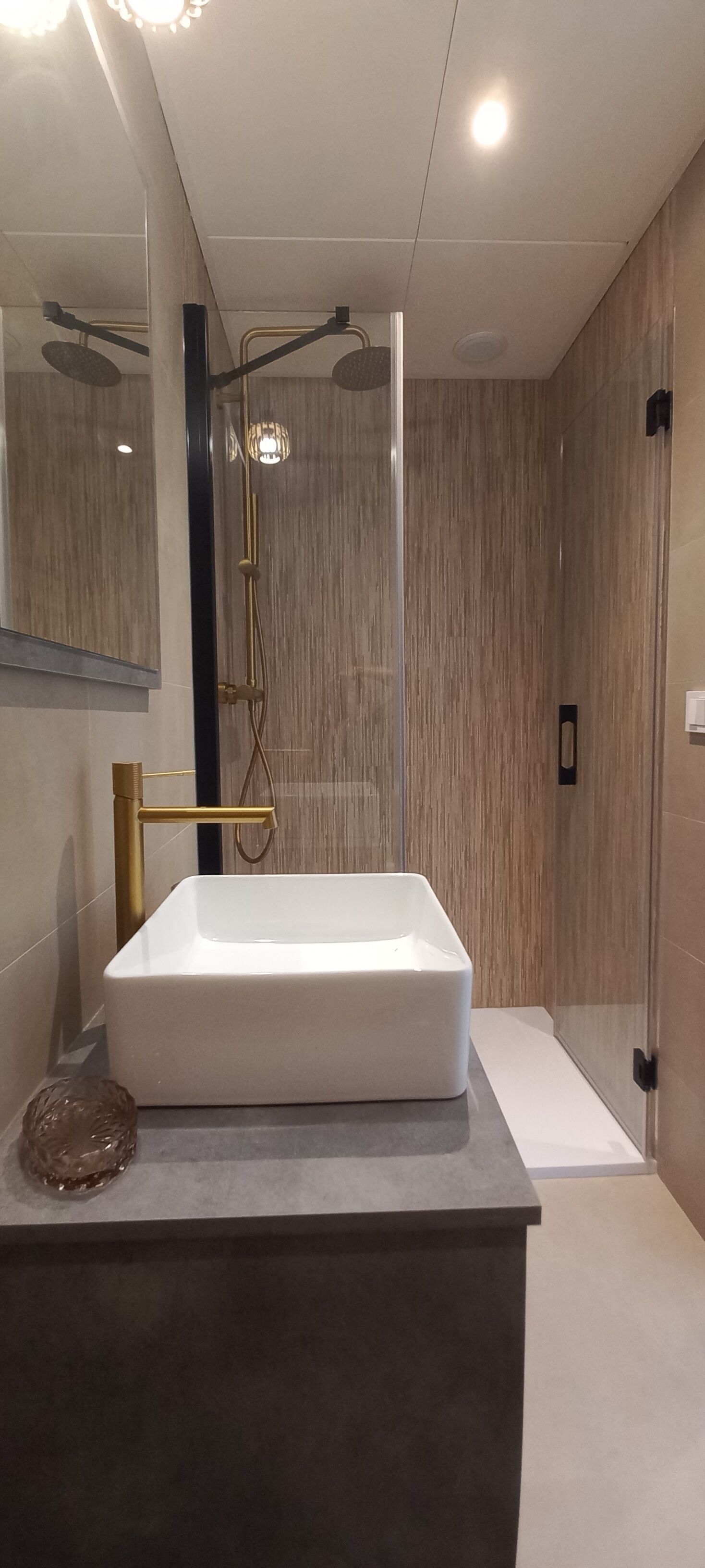 Een moderne badkamer met een rechthoekig wit wastafelmeubel, een glazen douchecabine en een houten wand.