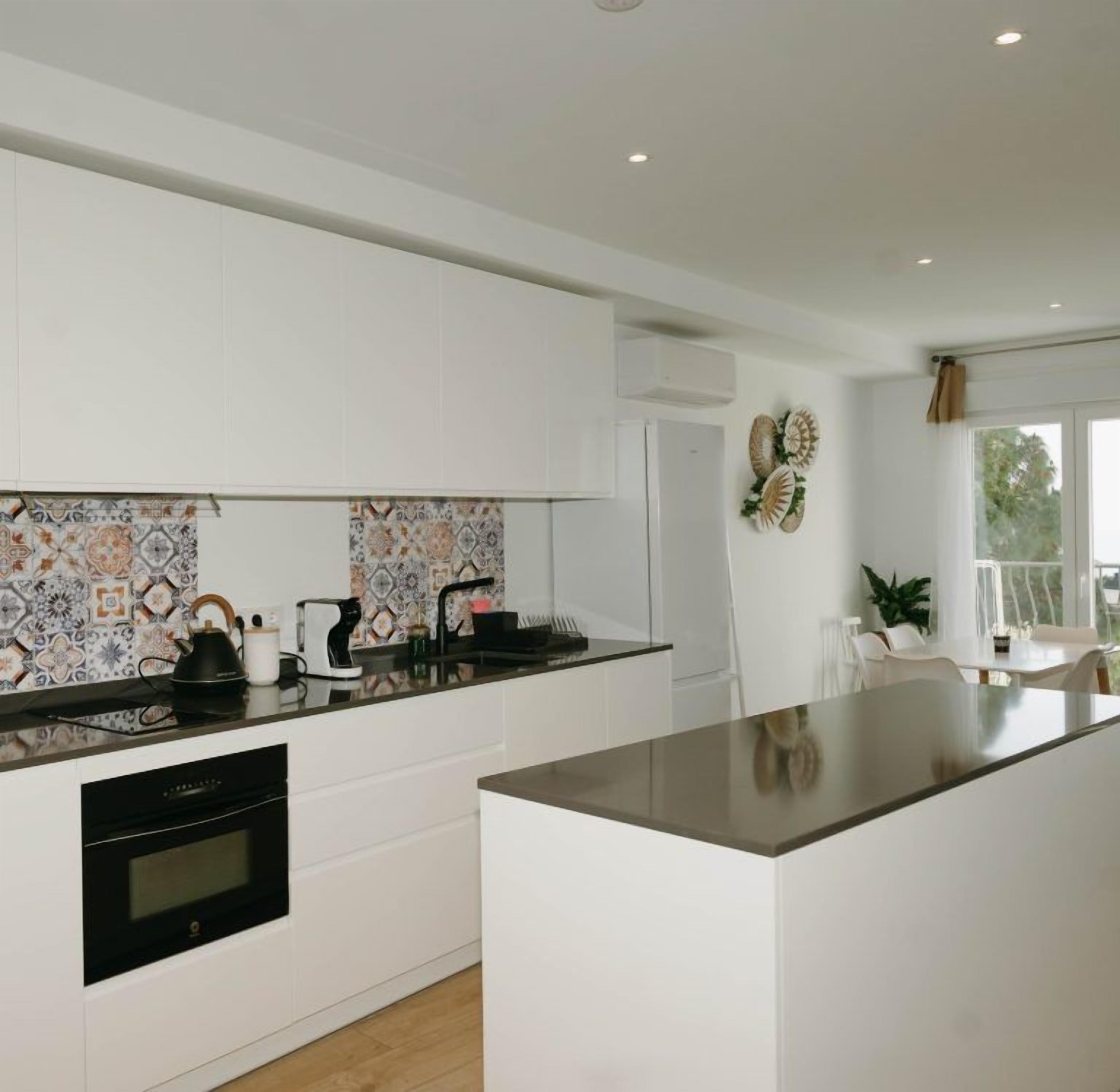 Una cocina moderna con armarios blancos, un salpicadero decorado y una isla central.