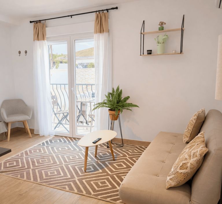 Un salon avec un canapé, une petite table, une plante en pot et un balcon doté d’une balustrade.