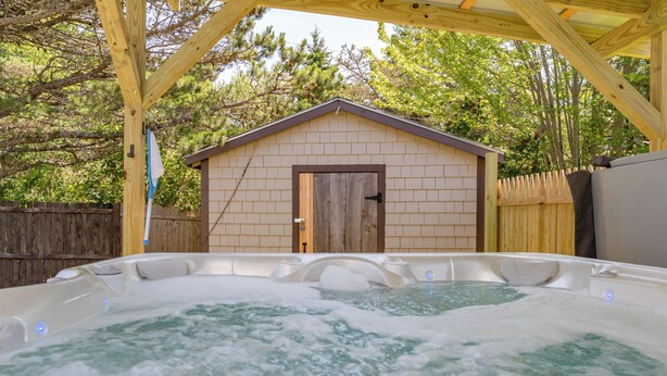 A hot tub with a wooden deck and a small shed in the background.