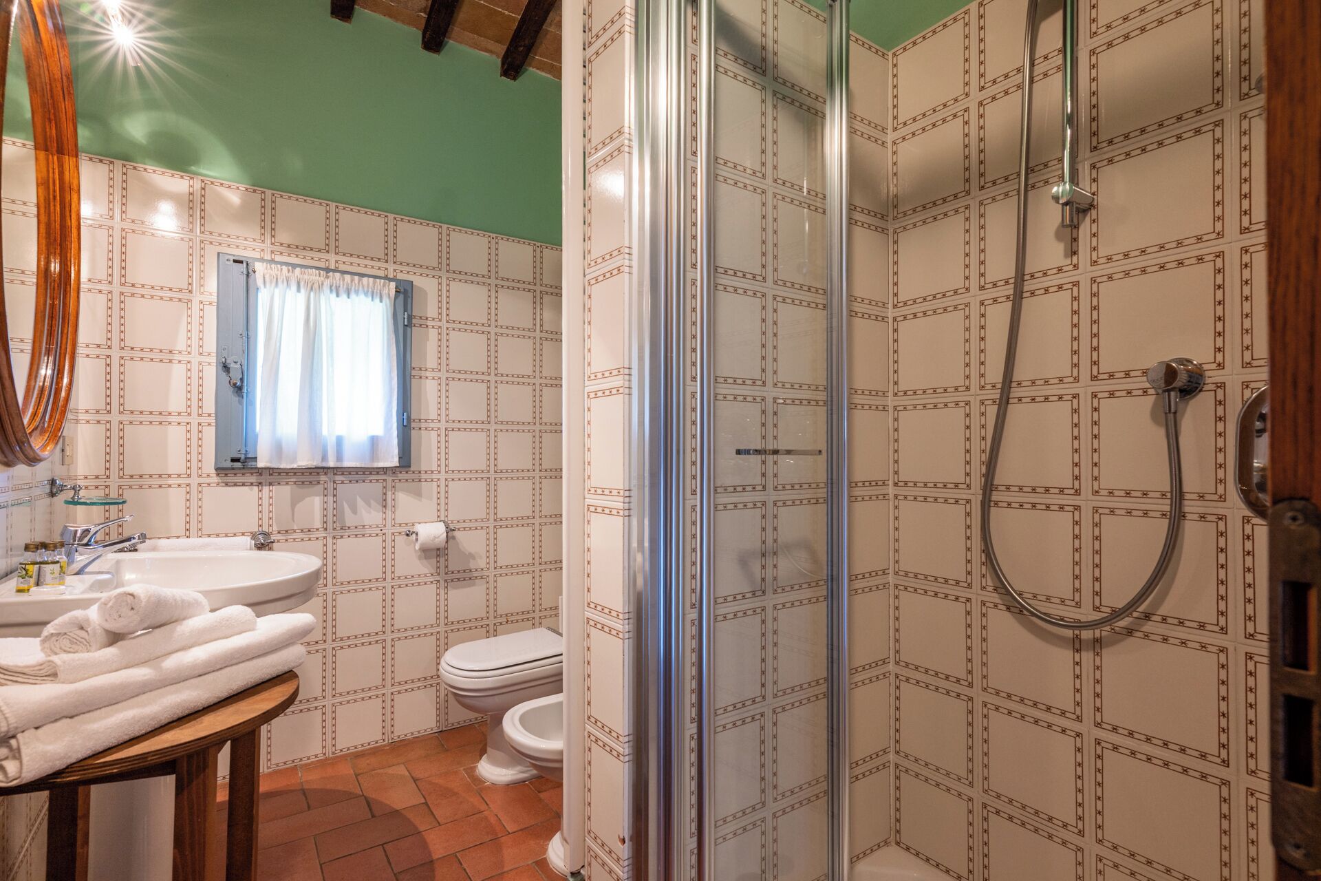 A bathroom with a shower, toilet, sink, and a window with curtains.