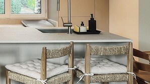 Eine moderne Küche mit großem Fenster, integriertem Spülbecken und einer Bar mit zwei Korbstühlen.