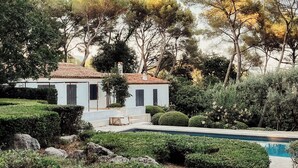 Eine weiße Villa mit einem Ziegeldach, umgeben von üppigem Grün und einem Swimmingpool.