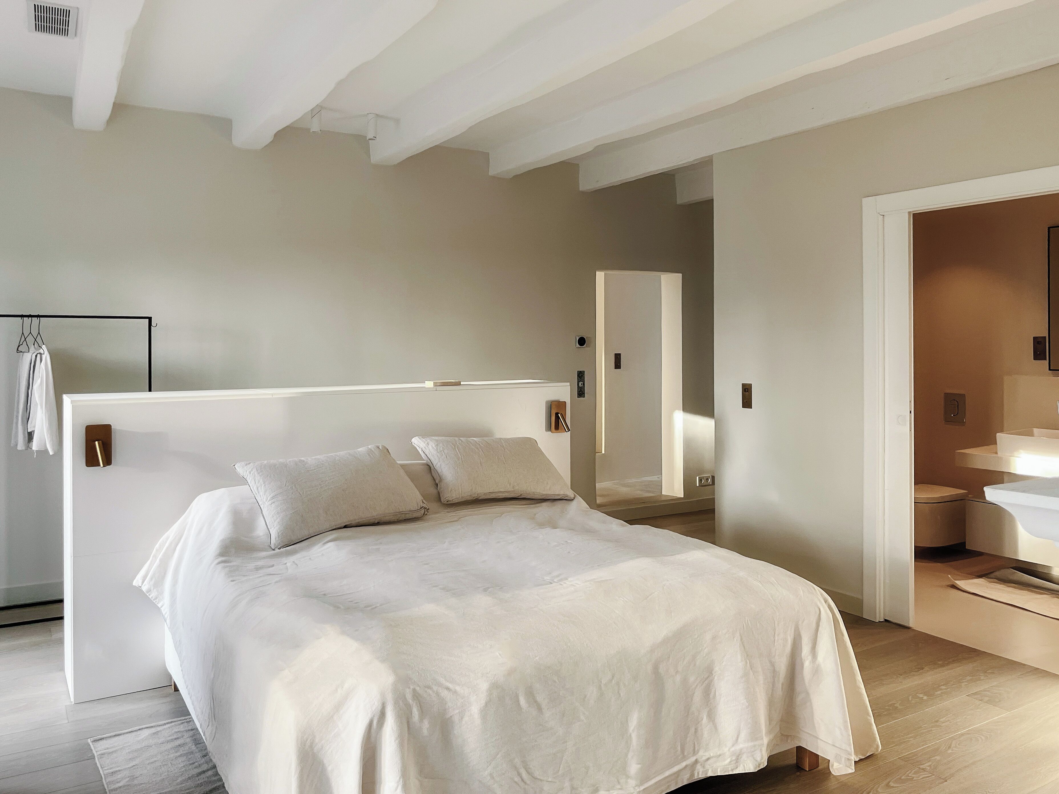 A modern bedroom with a large bed, a walk-in closet, and a bathroom with a sink and toilet.