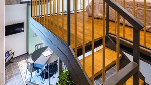 Un loft moderno con vigas de madera a la vista, una escalera, una zona de comedor y un dormitorio con cama y mesita de noche.