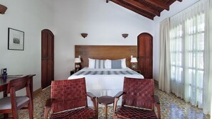Una habitación de hotel con una cama grande, dos sillones, un escritorio y una ventana con cortinas.
