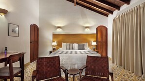 Habitación de hotel con una cama grande, dos mesitas de noche con lámparas, un escritorio con silla y una ventana con cortinas.