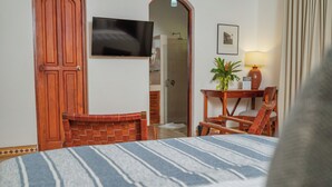 Habitación de hotel con cama, televisión, escritorio con lámpara, silla y planta en maceta.