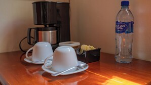 Une table en bois avec deux tasses blanches et une cuillère, une bouteille d’eau et un petit récipient contenant des mouchoirs.