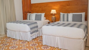 Une chambre d’hôtel avec deux lits, une tête de lit en bois, un tapis à motifs et une table de chevet avec une lampe.