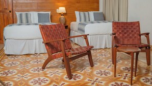 Une chambre d’hôtel avec deux lits, une tête de lit en bois, un sol à motifs et deux chaises en bois.