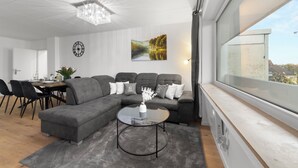 A modern living room with a sectional sofa, a glass coffee table, and a dining area with a table and chairs. - VlNFUL2: Premium apartment | balcony | parking space (Mülheim an der Ruhr)