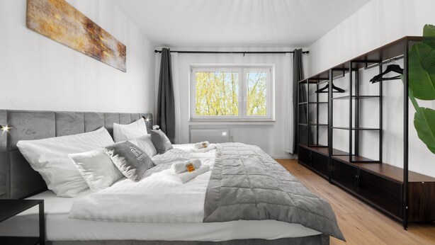 A modern bedroom with a bed, a wardrobe, and a window with a view of trees. - VlNFUL2: Premium apartment | balcony | parking space (Mülheim an der Ruhr)