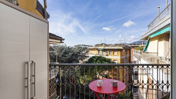 A balcony with a red table and chairs, overlooking a cityscape with buildings and trees. - La Poetessa With Pool by Wonderful Italy (Camogli)