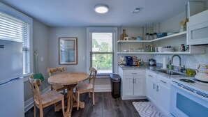 Une cuisine avec des meubles blancs, une table à manger en bois et une fenêtre avec des stores.