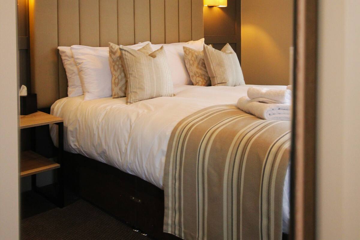 Ein Hotelzimmer mit einem großen Bett, einem Kopfteil mit Wandleuchten, einem Nachttisch und einem Teppichboden.