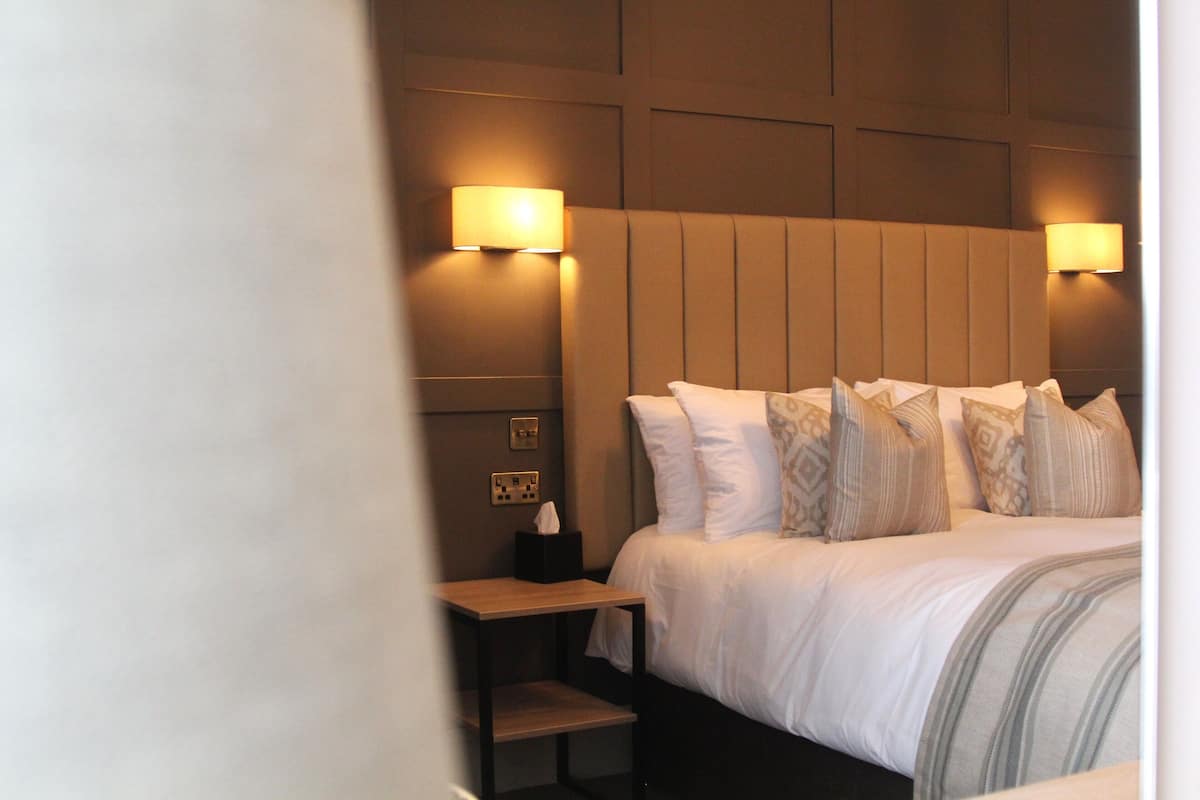 Ein Hotelzimmer mit einem großen Bett, zwei Nachttischlampen, einem Nachttisch und einem an der Wand montierten Lichtschalter.