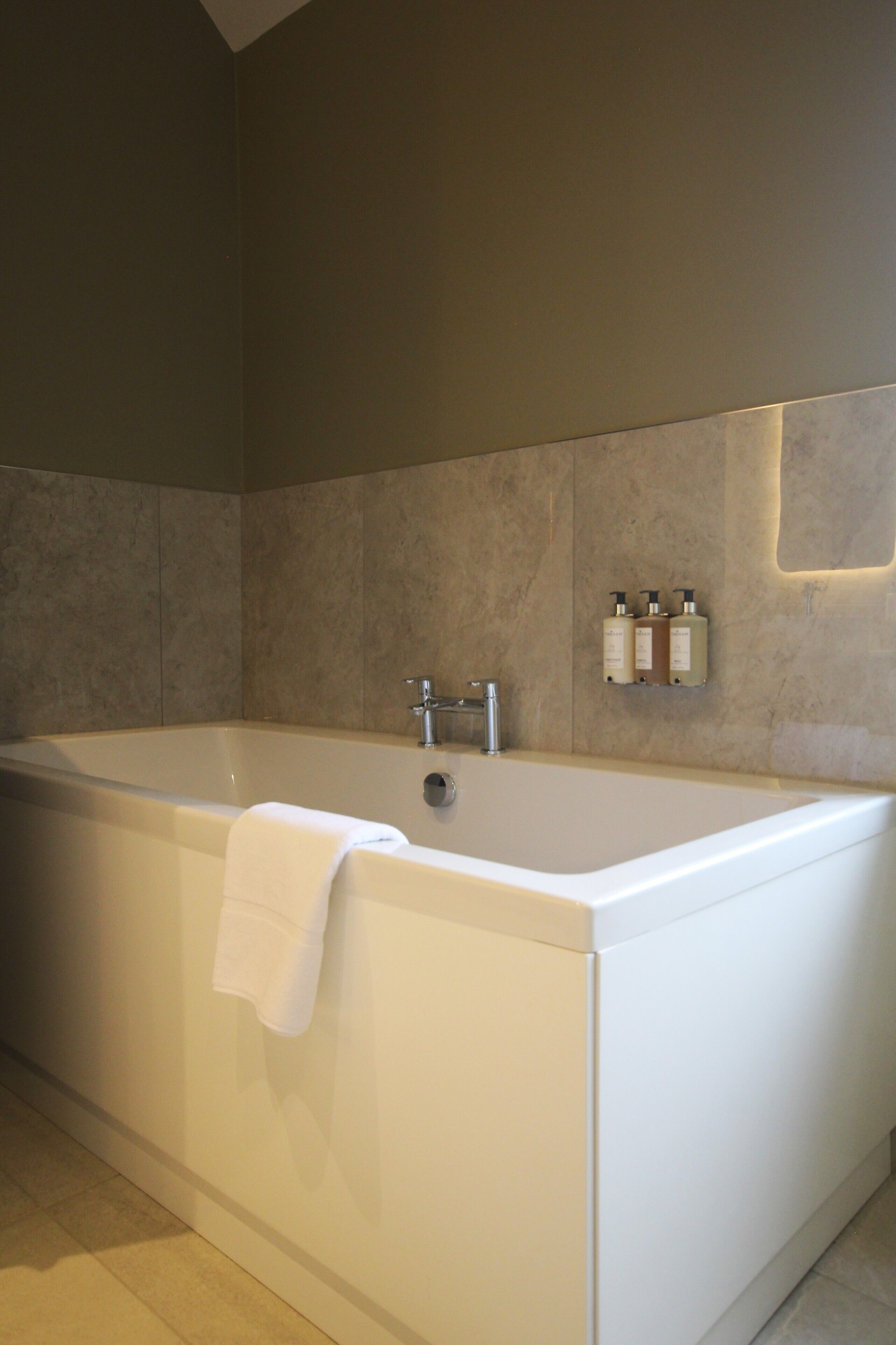 A modern bathroom with a large bathtub, a towel hanging on the side, and three bottles of toiletries on the wall.