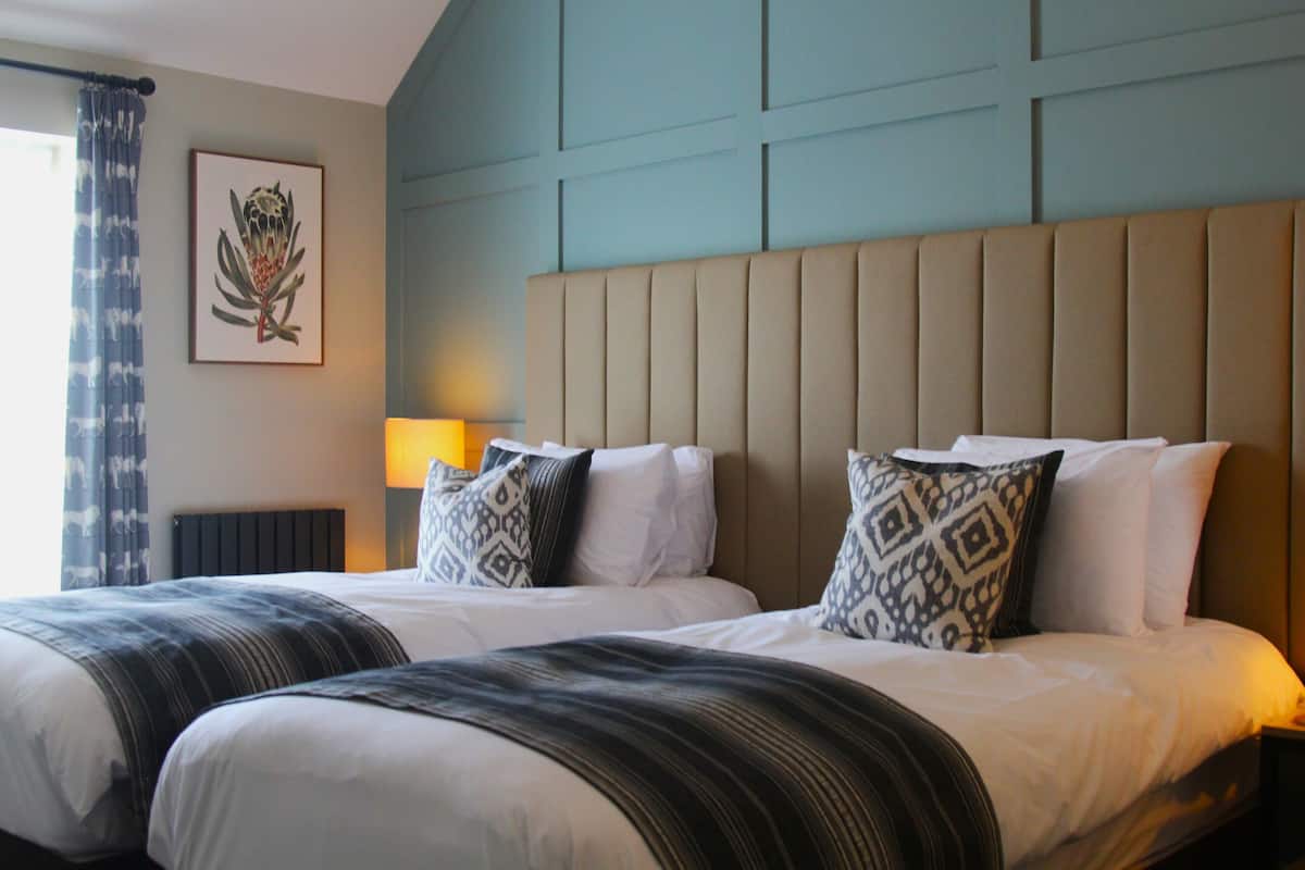 Ein Hotelzimmer mit zwei Betten, einem Kopfteil, einer Lampe und einem gerahmten Bild an der Wand.