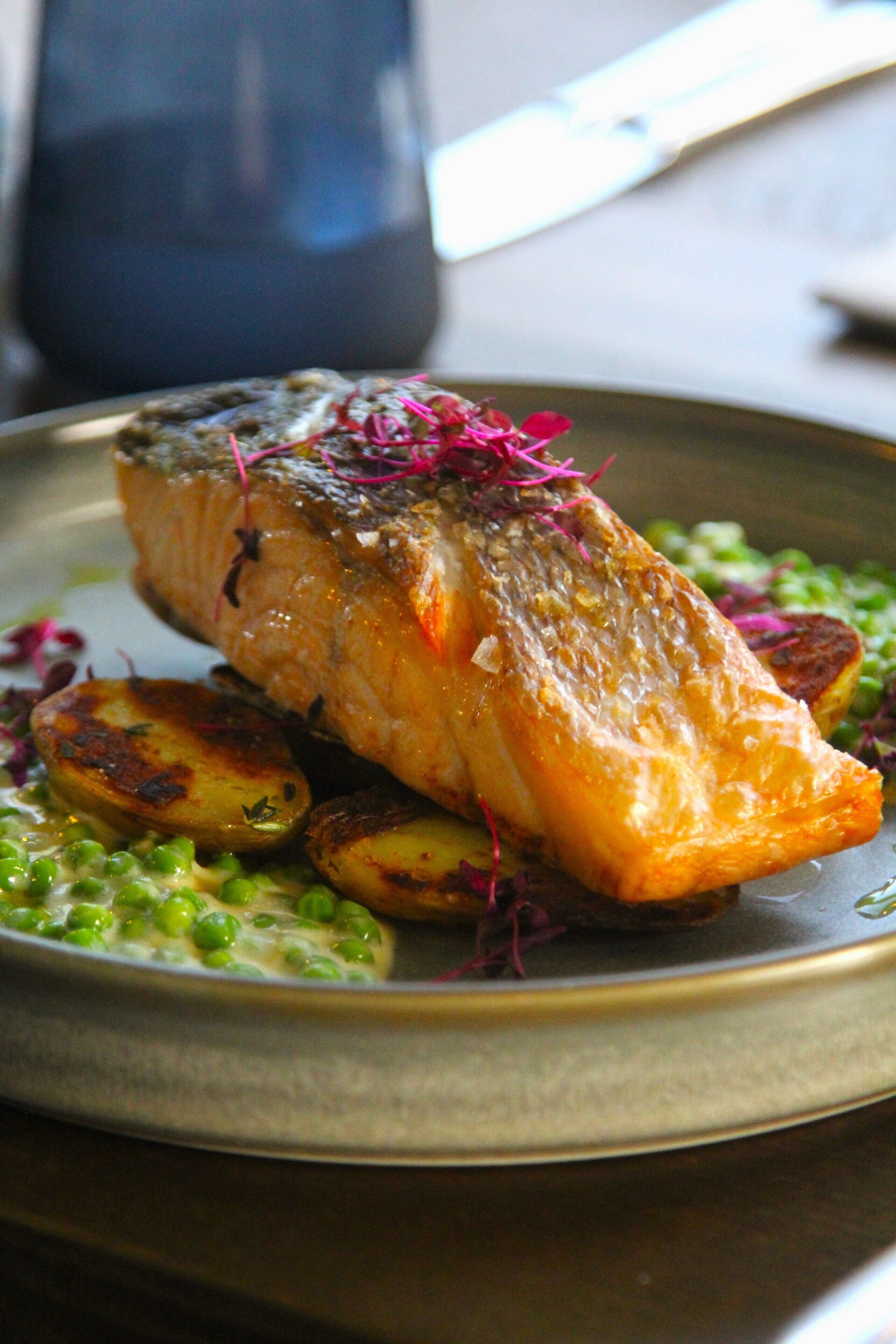 Un piatto con salmone, patate arrosto, piselli e guarnizione.