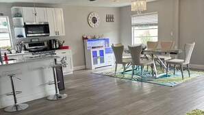 A modern kitchen with white cabinets, a microwave, and a coffee maker. There is a dining area with a table and chairs, and a large window providing natural light.