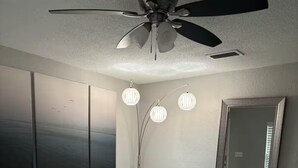 A modern living room with a white leather sofa, a glass coffee table, a ceiling fan, and a large mirror on the wall.