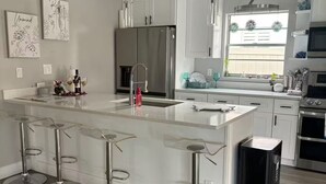 A modern kitchen with a central island, bar stools, stainless steel appliances, and a window with decorative plants.