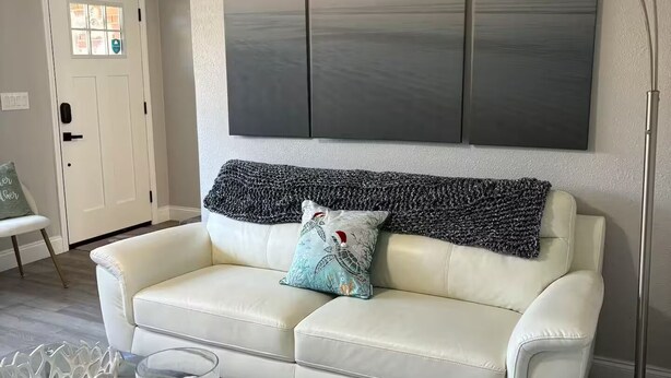 A modern living room with a white leather sofa, a glass coffee table, a large abstract painting, and a floor lamp.