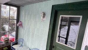 En veranda med två blå stolar av metall, ett litet bord och en grön dörr med ett fönster.