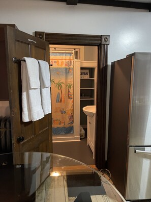Una cucina con una porta in legno, un frigorifero in acciaio inossidabile, un lavandino bianco e una tenda da doccia colorata.