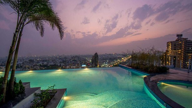 A rooftop infinity pool with a cityscape view at dusk.