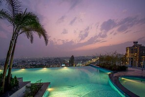 A rooftop infinity pool with a cityscape view at dusk. - The Grand Anukampa Hotels & Suites (Jaipur)